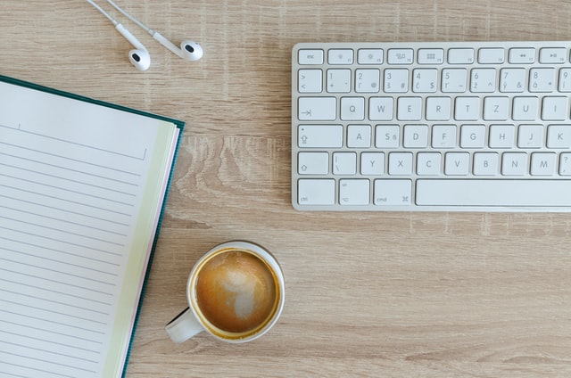 desk with keyboard, journal, coffee, and headphones